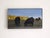 In "Evening Glow," two silhouetted cows graze peacefully in a sunlit field, their dark forms contrasting against the warm,...