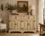 Charming vintage French Provincial-style wooden sideboard or buffet cabinet featuring an aged, distressed cream/off-...