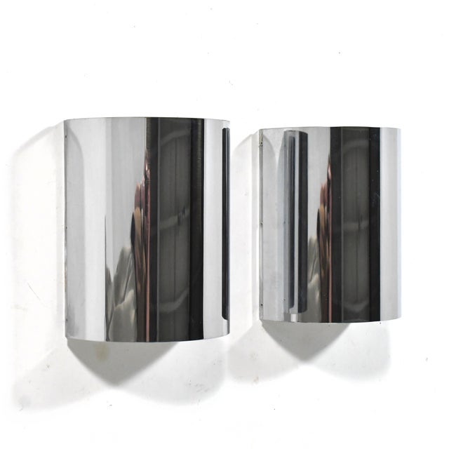 This pair of elegant, minimalist wall sconce lamps feature chrome-plated semi-circular-shaped steel shades concealing two...
