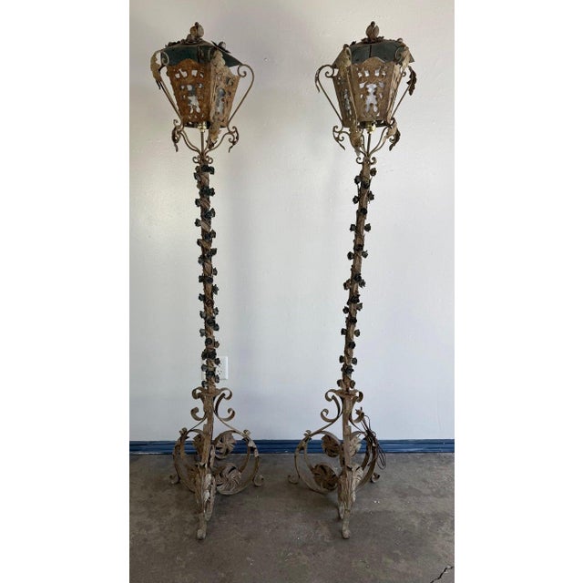 These are a pair of vintage wrought iron floor lanterns with an ornate and rustic aesthetic. The design features intricate...