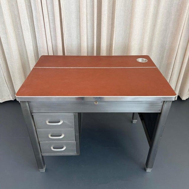 This mid-century, industrial, brushed steel military desk circa 1940s features a newly clad, rust brown textured leather...