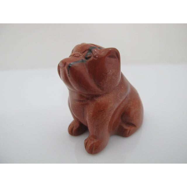Hand-carved red jasper gemstone figurine of a seated bulldog, recognizable by its wrinkled face and stocky build. Polished...