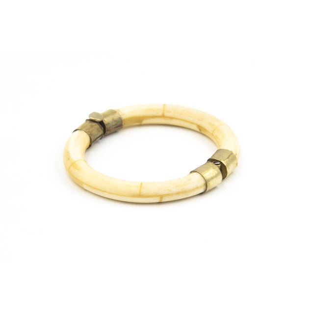 A smooth, rounded bone bangle bracelet in a warm ivory-yellow tone, accented with decorative gold-tone metal bands and...