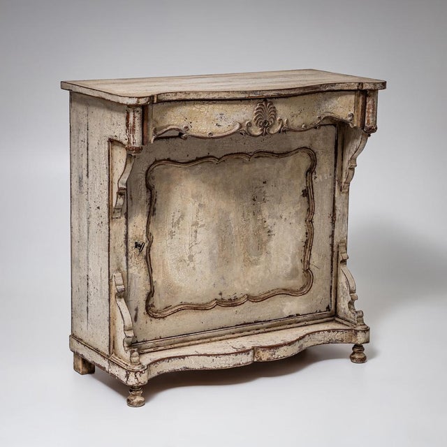 Half cabinet with a single door featuring a shaped panel, curved corner ornaments, and a drawer with carved shell...