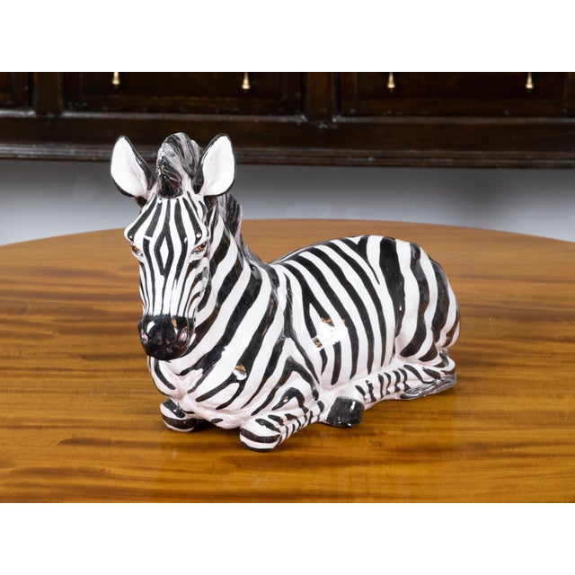 A small vintage Italian hand painted terracotta animal sculpture depicting a zebra lying on the ground, with brown eyes....