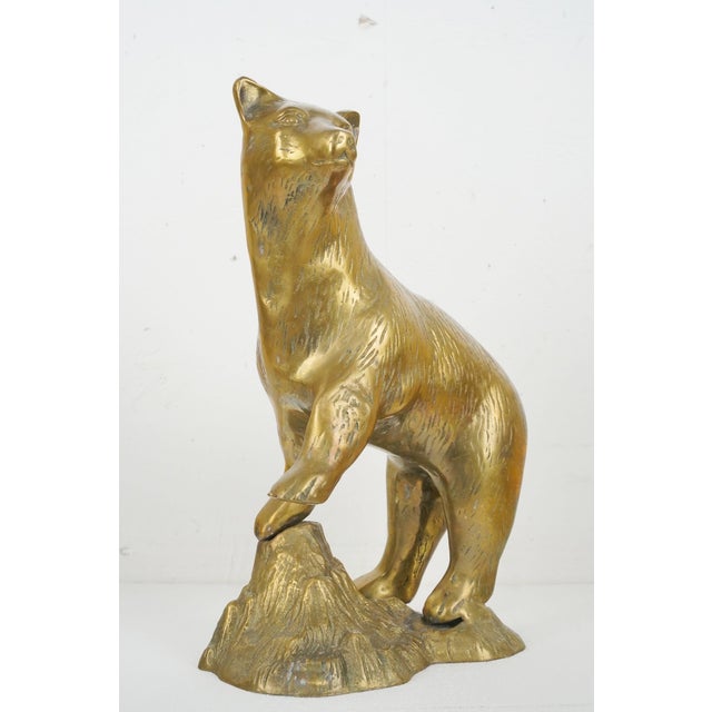 Vintage brass black bear standing proudly with its right front paw elevated onto a rugged, textured rock formation. Great...