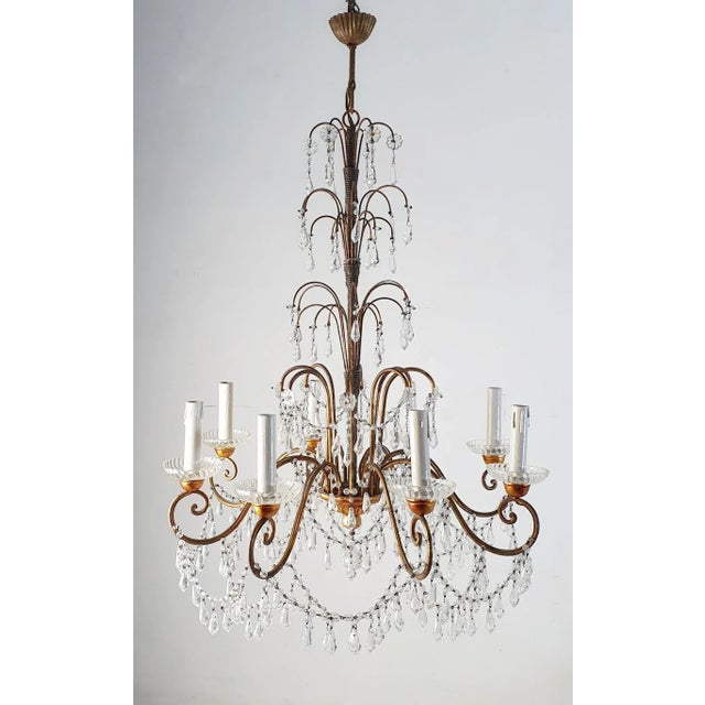 An Italian crystal chandelier in Empire style made with a gilded structure adorned with swags of crystals that glitter...