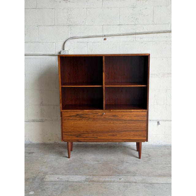 This beautiful storage unit features an upper open display layout with shelves sitting above a lower drop-front cabinet....