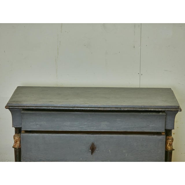 A French Empire style painted wood four-drawer commode from the 19th century with ebonized columns, carved giltwood female...
