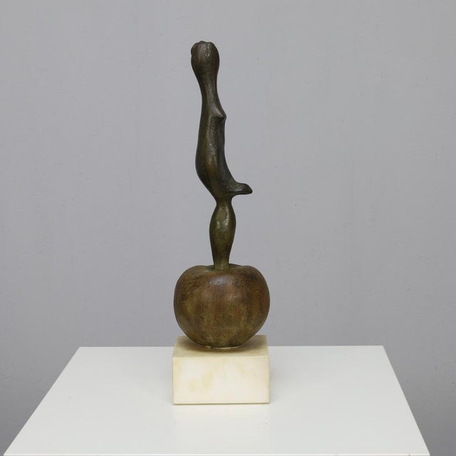 Highly abstracted female figure balanced on top of a rounded apple form. The composition is vertical and totemic, rendered...