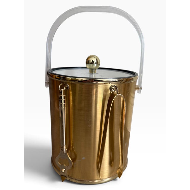 Striking vintage 1970s ice bucket in a glamorous gold-tone finish, featuring a clear Lucite swing handle, matching Lucite...
