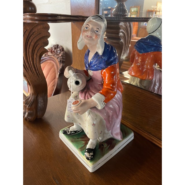 Antique 19th century Staffordshire figure depicting the Cobbler's Wife in a seated position pouring a jug. Dominant colors...