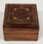 Petite wood hinged trinket box with brass inlay to top framing a hand carved flower. Age wear.