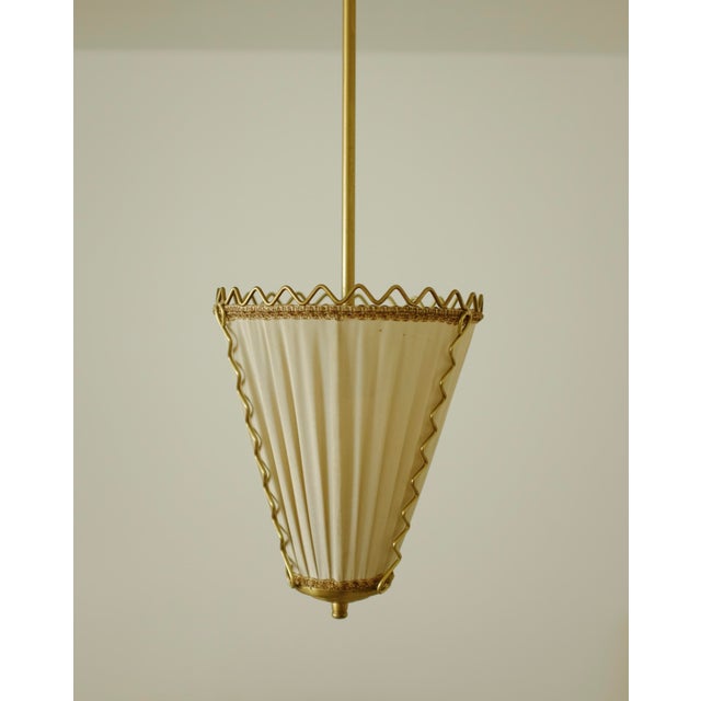 Gorgeous Swedish 1950s Brass and Silk pendant. One light source with a brass lamp arm and frame that is decorated with a...