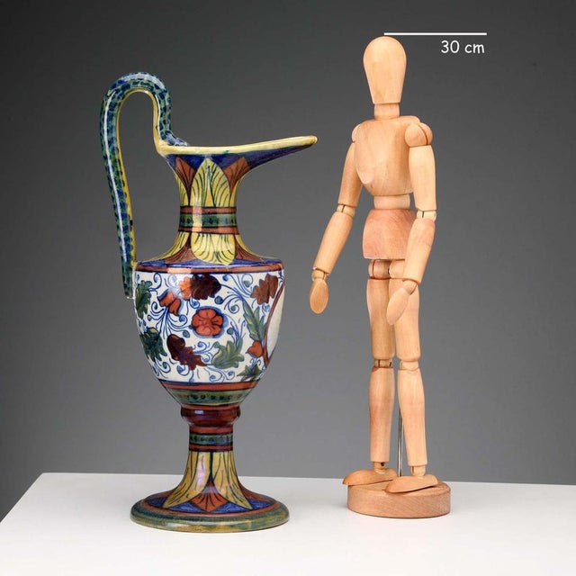 A glazed majolica jug with an ovoid body and a saddle-shaped handle shaped like a serpent. The belly features a medallion...