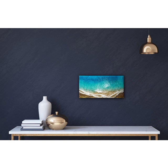 This mixed media piece on wood panel captures the serene beauty of a beach scene, where vibrant turquoise waves gently...