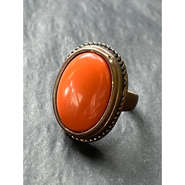 Vintage costume cocktail ring with a bold coral-hued resin stone set in a bronze-tone metal. The oversized setting and...