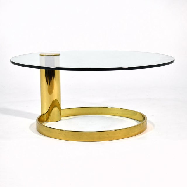 This handsome coffee table features a brass base with a single offset column that supports a round cantilevered glass top....
