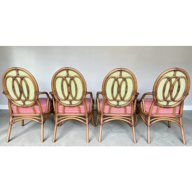 A set of four vintage rattan dining armchairs featuring sculptural oval medallion backs and gracefully curved arms. The...