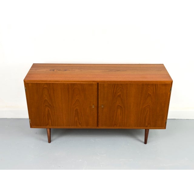 Compact and practical teak sideboard with two lockable cabinet doors. The interior is veneered in light maple and features...
