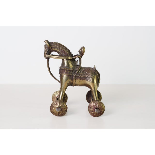 An antique hand-cast brass horse with mounted rider on four ornately decorated wheels, in the Indian temple toy tradition....