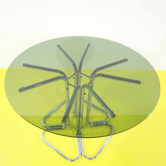 Round table featuring a smoked glass top and a chrome tubular structure.