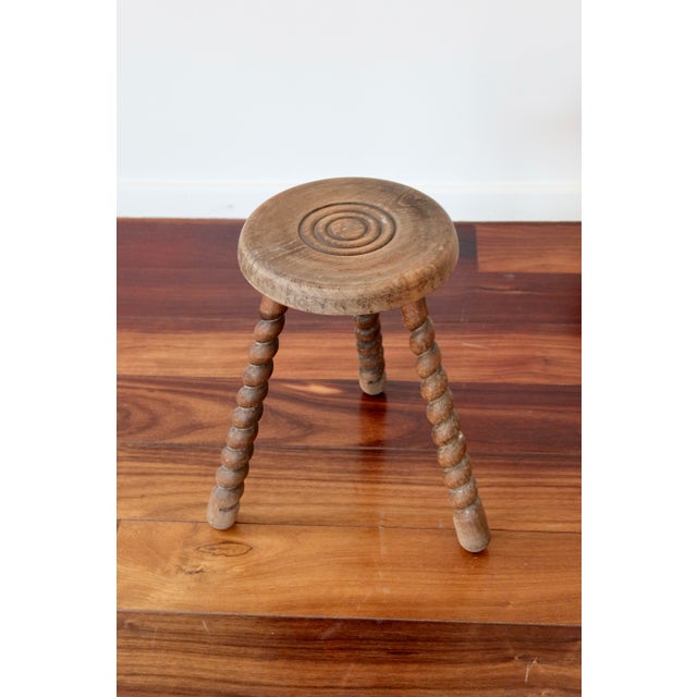 Antique tripod stool in solid wood, with a spirally turned base and a round seat marked with concentric circles, typical...