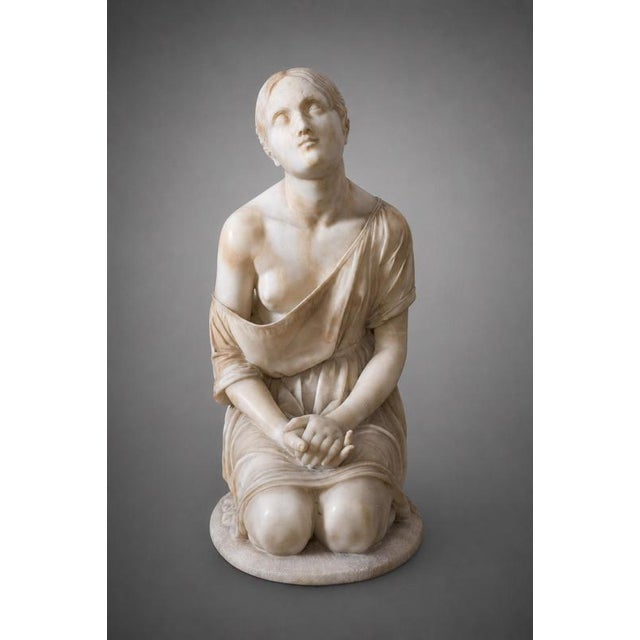 An antique alabaster sculpture depicting a kneeling female figure in the round. Lombardy, 19th century. The composition is...