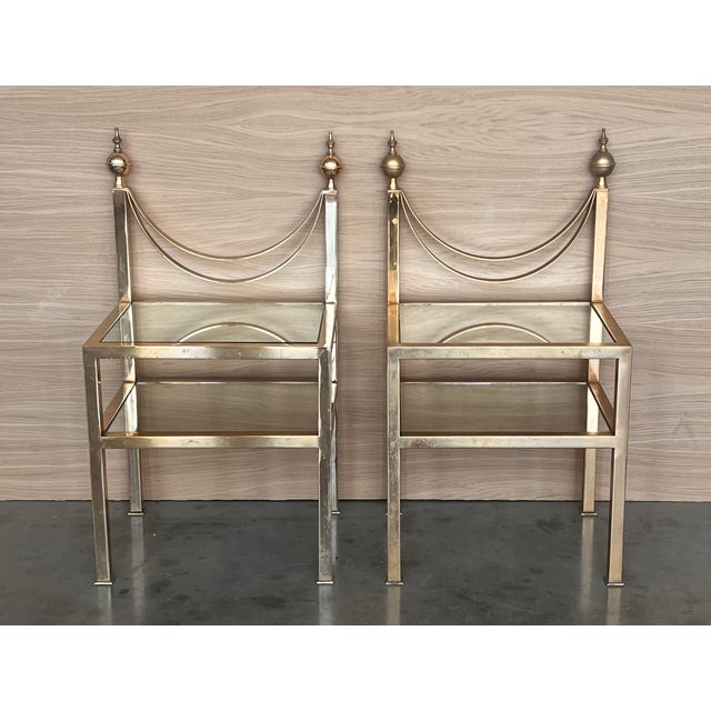 Pair of midcentury Italian two tier brass and glass nightstands with crest. Simple tables with a low grid shelve and glass...