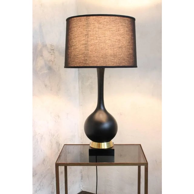 A handsome American Mid-Century table lamp dating to the 1960s, featuring a sculptural matte black ceramic body resting on...