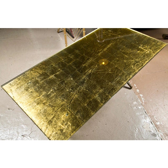 A chic coffee table of Hollywood Regency taste, the gold-leaf rectangular glass top supported on a gilt-brass base with a...