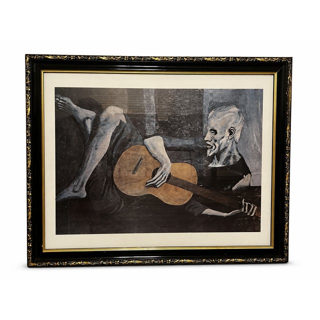 Framed reproduction of Pablo Picasso’s celebrated The Old Guitarist, originally painted in Barcelona in 1903–1904 during...