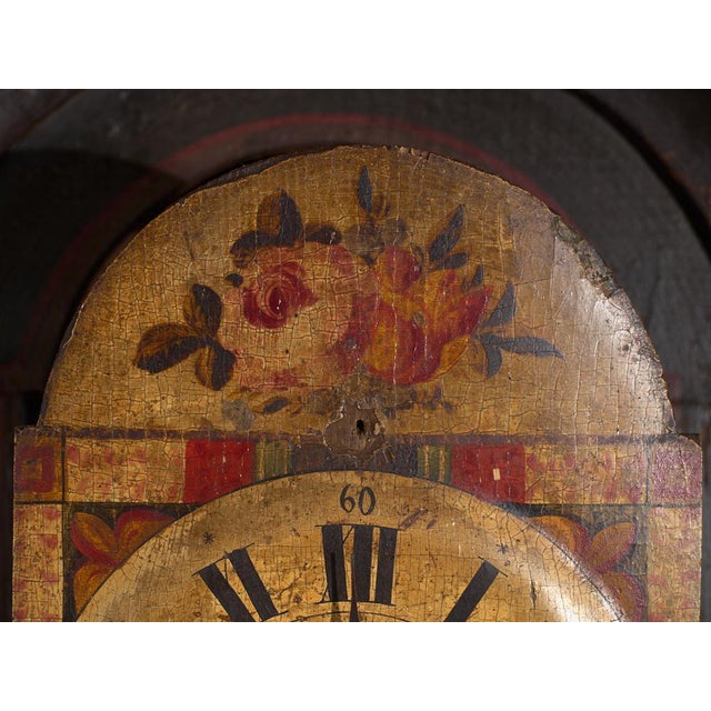 This antique longcase clock rises on a solid pine case painted in dark green, with two painted panels of floral sprays...