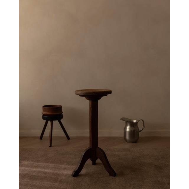 Vintage wooden pedestal plant stand with a slim, tall silhouette and round top. The tripod base and dark-stained wood give...