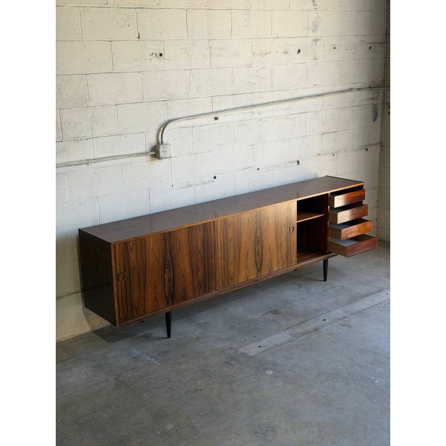 This minimalist lowboard features a long rectilinear frame elevated by tapered peg legs. The four sliding doors glide open...