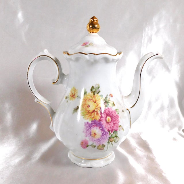 This is a Winterling coffee pot in an unknown pattern name. It is white with gold trim, scalloped rims and pink, purple,...
