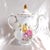 This is a Winterling coffee pot in an unknown pattern name. It is white with gold trim, scalloped rims and pink, purple,...