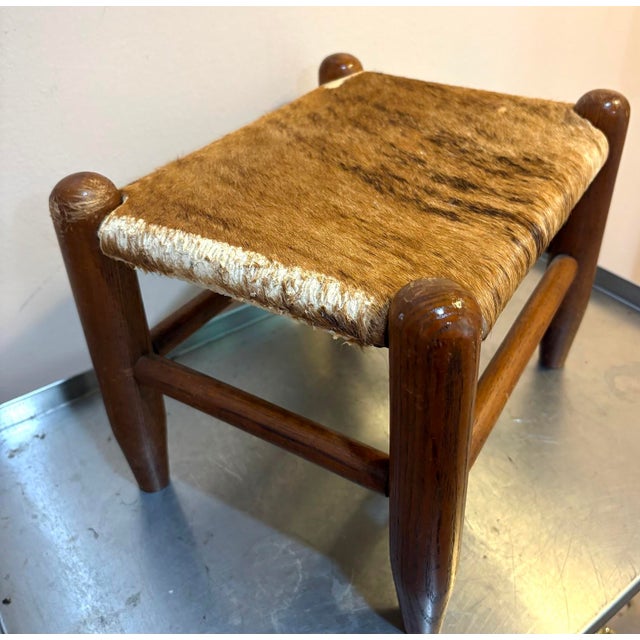 1950s-60s midcentury wood/cowhide footstool. Cowhide has some surface wear on the edges in a few places as shown.