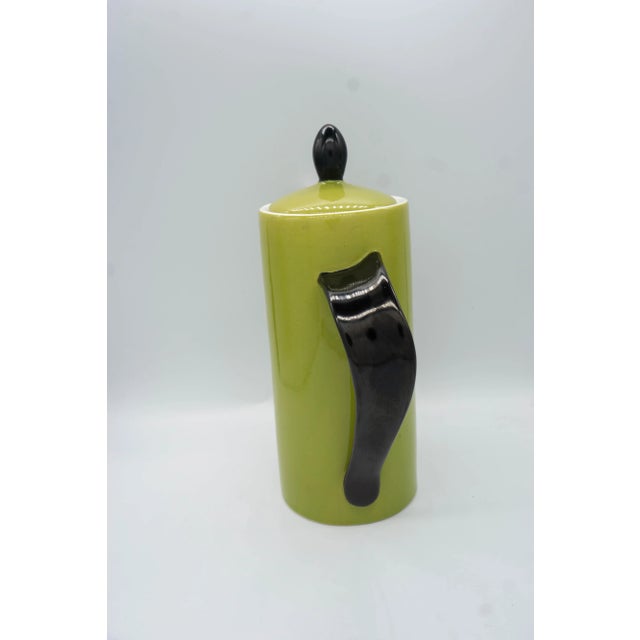 Tall tea pot, green with black accents, no markings. Handle has an ergonomic, asymmetric twist Dimensions: 8 1/4" Height...