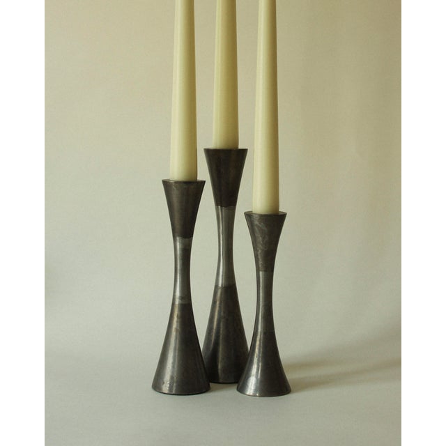 Three candleholders of varying heights, crafted from weathered steel and brushed in the central section to create a...