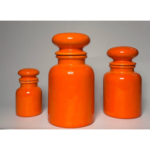A bright, fluorescent orange colored paint with a glossy finish adorn this set of three, (3), vintage apothecary jars....