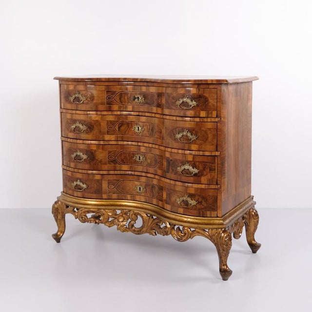 Antique Baroque chest of drawers crafted in polished walnut and fitted with four drawers, decorative brass handles, and...