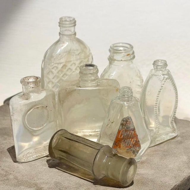 Collection of seven tiny vintage glass bottles in an assortment of shapes and sizes, originally used for cosmetics,...