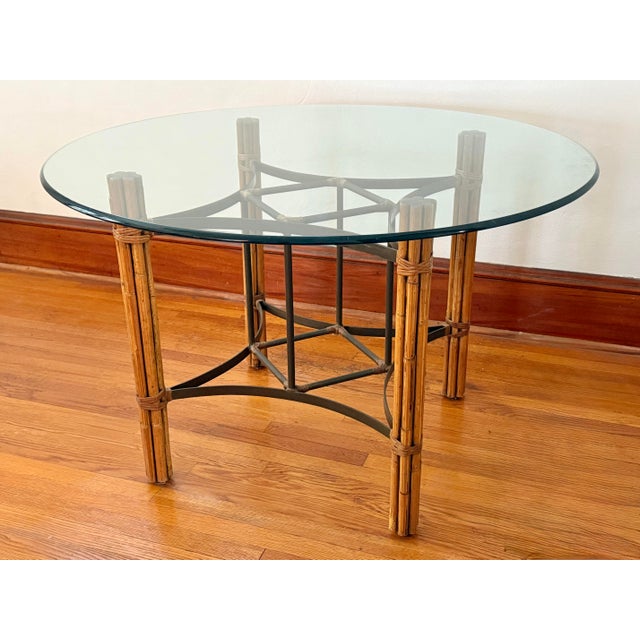 This vintage dining table has a round glass top resting on a base of rattan and bamboo legs wrapped in rawhide. A black...