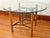 This vintage dining table has a round glass top resting on a base of rattan and bamboo legs wrapped in rawhide. A black...