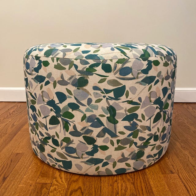 Custom round ottoman upholstered in Imogen Heath Evergreen fabric; botanical shapes travel across the surface of the...