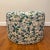 Custom round ottoman upholstered in Imogen Heath Evergreen fabric; botanical shapes travel across the surface of the...