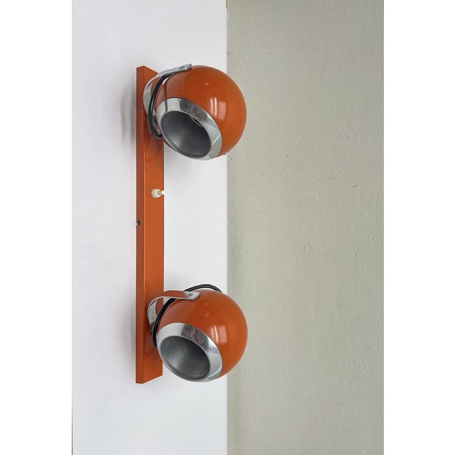 An orange with chrome details wall spotlight ‘double eyeball’ from the 1970s. You can light 1 spotlight or both with the...