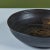 From famed Hawaiian ceramicist Toshiko Takaezu, a wheel thrown studio ceramic bowl features a dark brown glaze with tan...