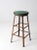 This is a vintage industrial work stool. The tall metal frame stool features a round green upholstered seat with red trim.